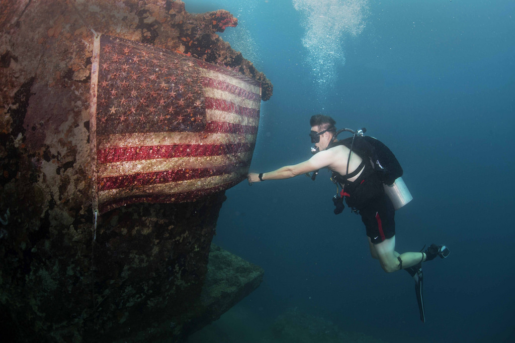 man scuba diving, shipwreck with American flag