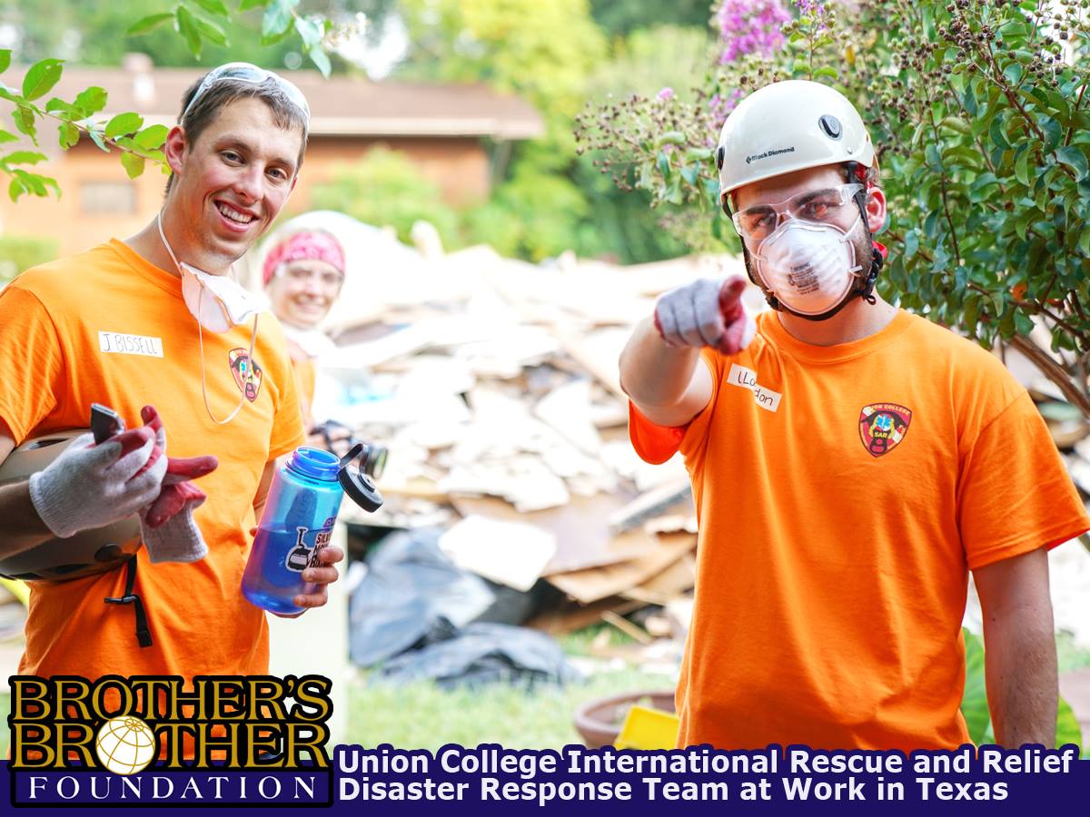 Two men in orange shirts and face masks, pile of construction rubbish behind them