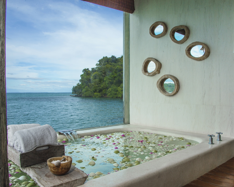 bathtub filled with flower petals, overlooking open window and ocean