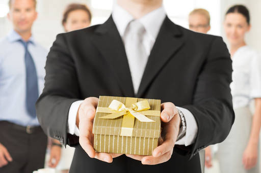 man in suit holding out boxed present with gold ribbon