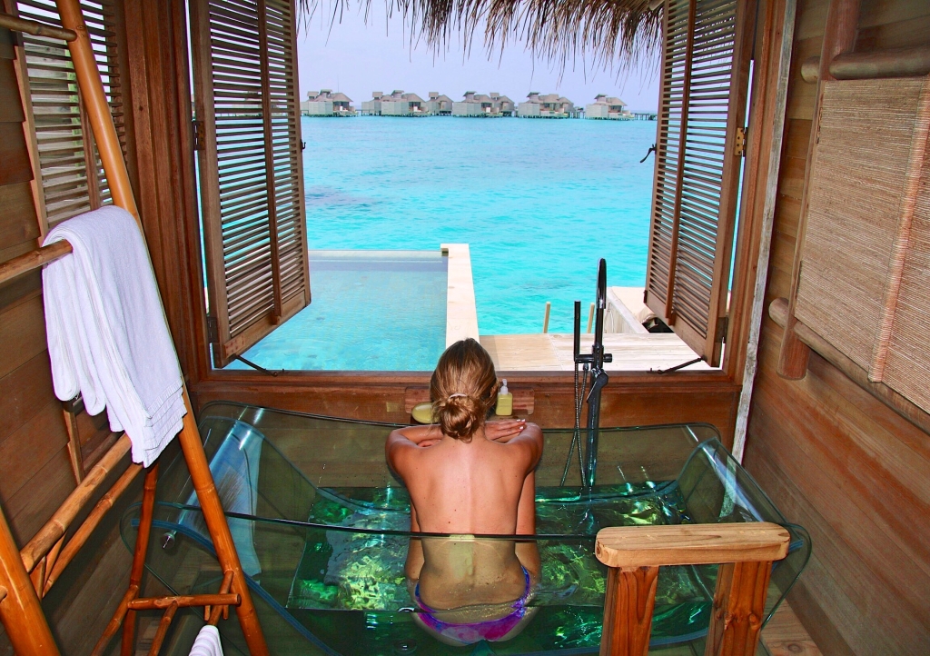 woman in glass-bottomed bath, over looking turquoise Indian Ocean water in Maldives