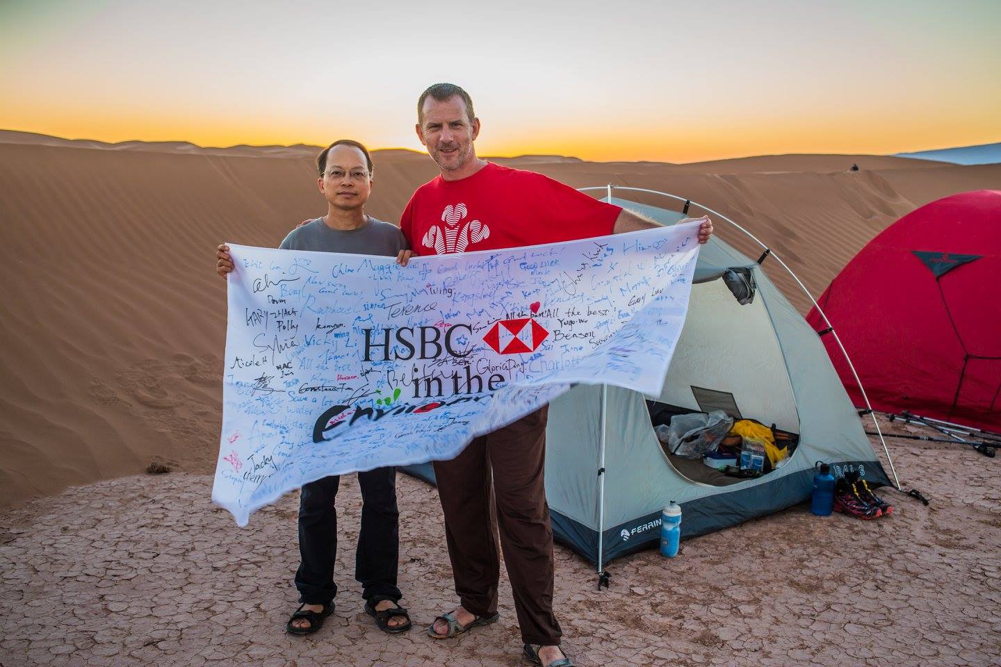 two men holding HSBC white banner with sunset over desert in background