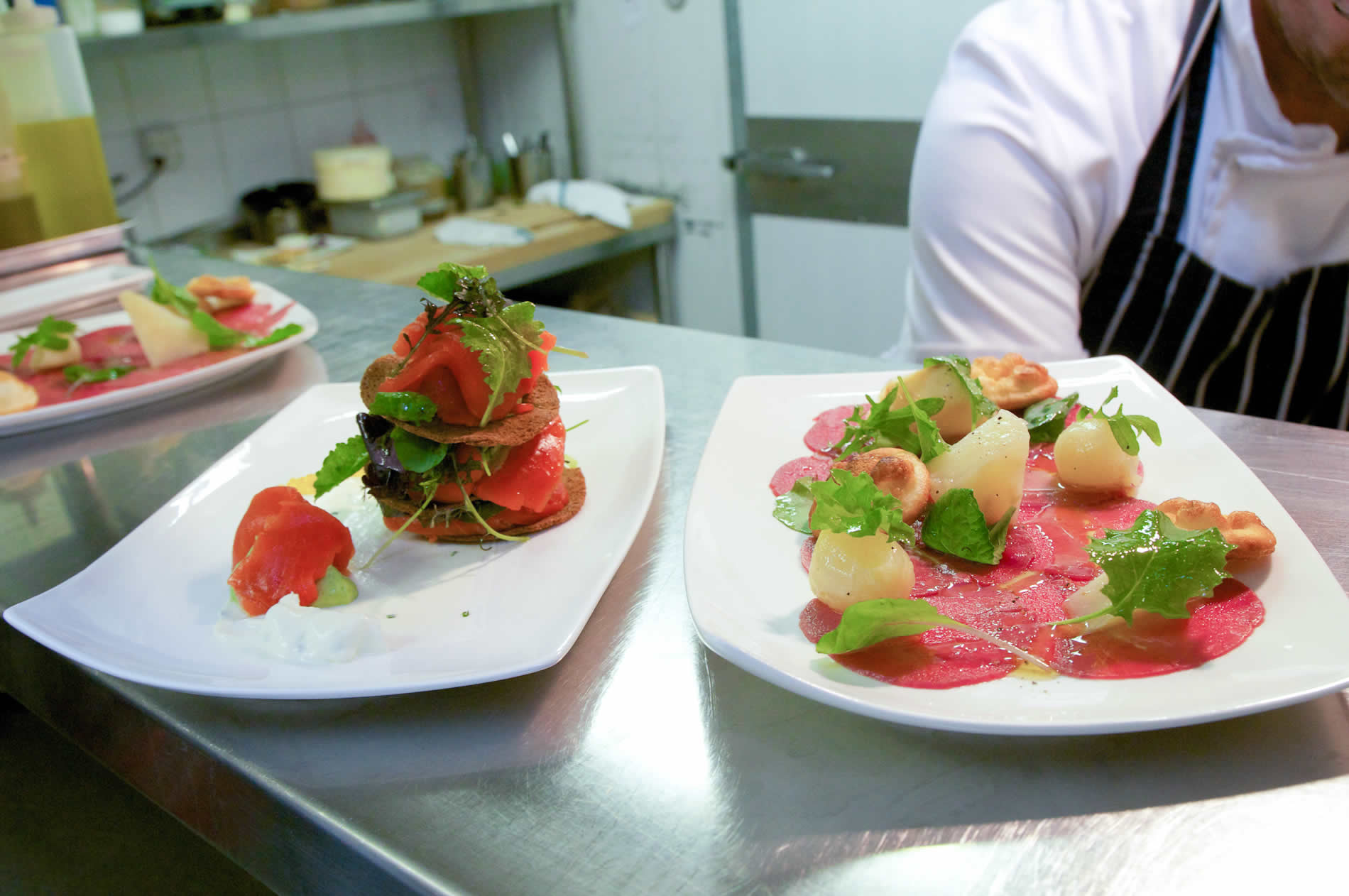 Two plates of carpaccio and piles of fish and fresh vegetables