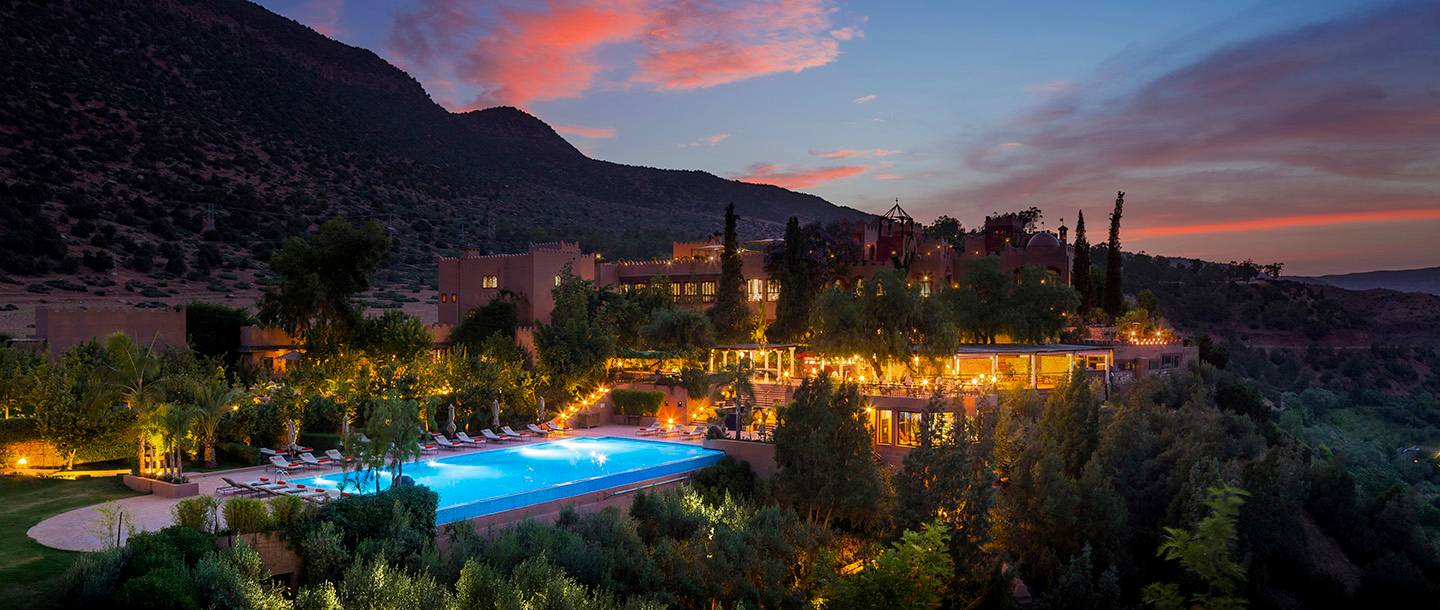 large hotel lit at night, blue pool, dusky sunset