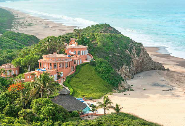 terracotta coloured villas perched on cliff with beaches and pacific ocean below