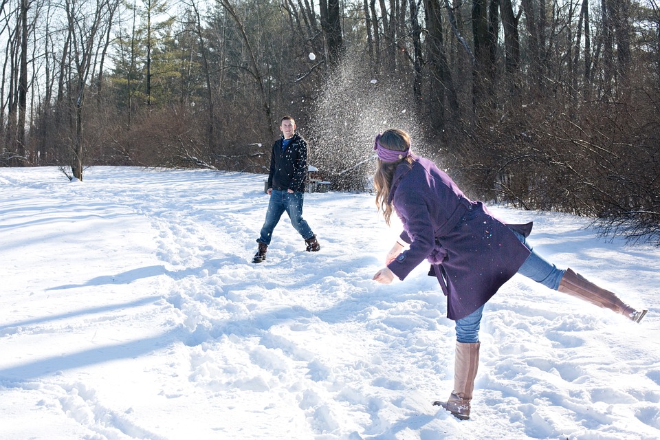 woman in purple coat throwing snowball at man